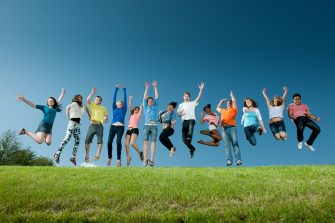 A large group of young adult college students jumping on a hill.