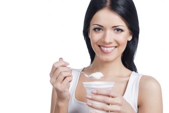 I love mornings. Beautiful young smiling woman holding a spoon with sour cream while standing against white background